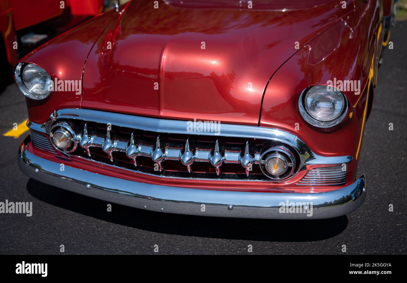 Front end of red restored antique vintage sedan automobile, including grille, bumper and headlights. Stock Photo