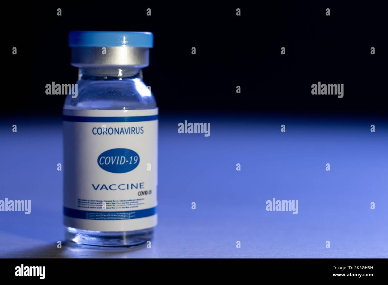 Coronavirus vaccine. Pandemic banner. Covid-19 inoculation. Healthcare industry. Blue dose vial glass bottle with label on defocused dark copy space b Stock Photo