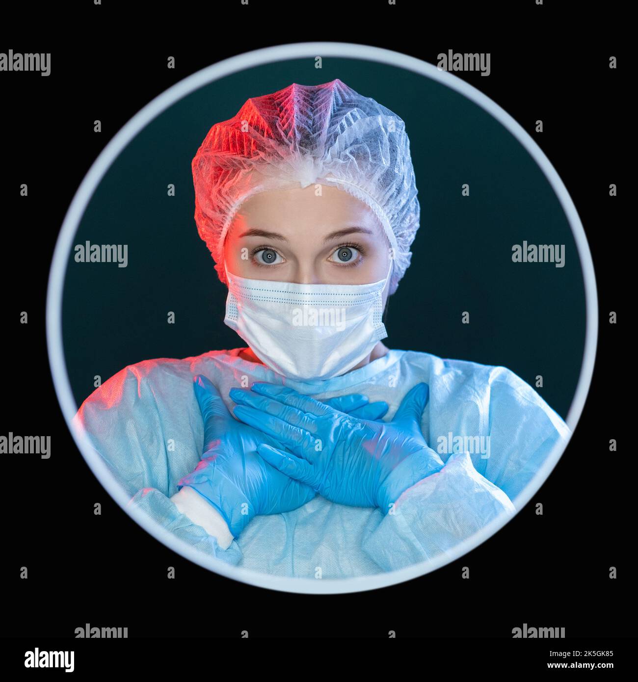 Shocked surgeon. Medic portrait. Unbelievable discovery. Portrait of speechless disturbed female doctor in blue ppe face mask gloves with hands at che Stock Photo