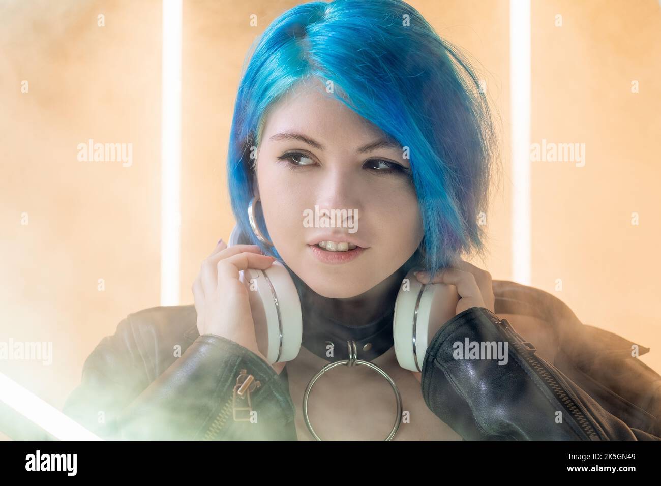 Woman DJ. Night life. Futuristic party. Pretty smiling cyberpunk young girl with headphones in LED lamp light smoke nightclub background. Stock Photo