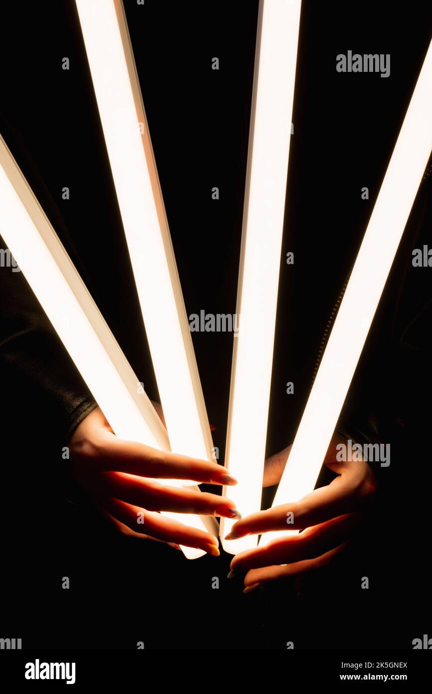 Light tube. LED illumination. Modern lighting. Closeup of female hands holding bright glowing fluorescent lamp isolated on black background. Stock Photo