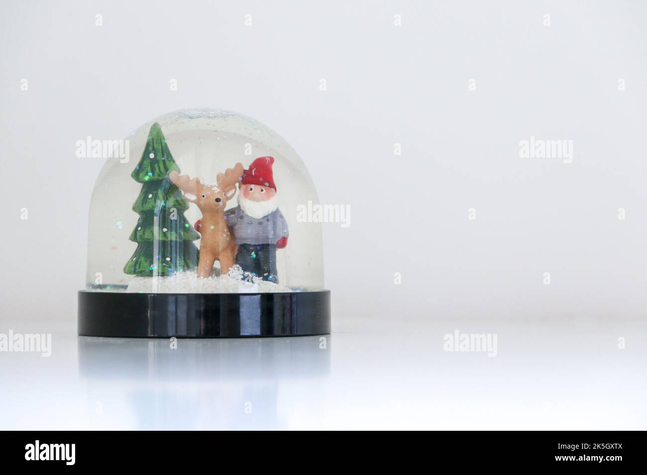 Christmas snow globe featuring Santa Claus, his reindeer and a Christmas tree, on white snowy background, festive ornament decoration, copy space on t Stock Photo