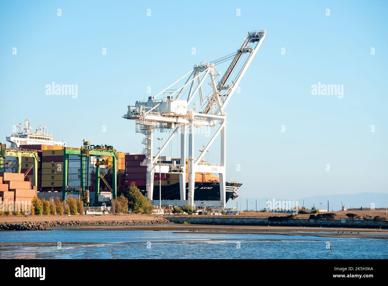 Cranes loading cargo containers on ship at Port of Oakland by bay on sunny day Stock Photo