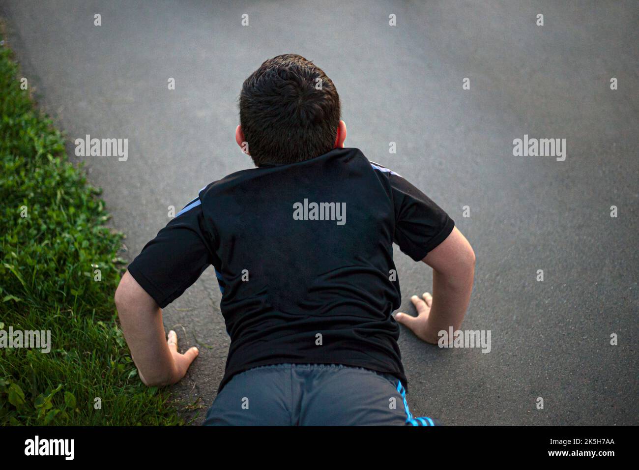 Child does push-ups from ground, Playing sports. Falling on asphalt. Boy is lying down. Stock Photo