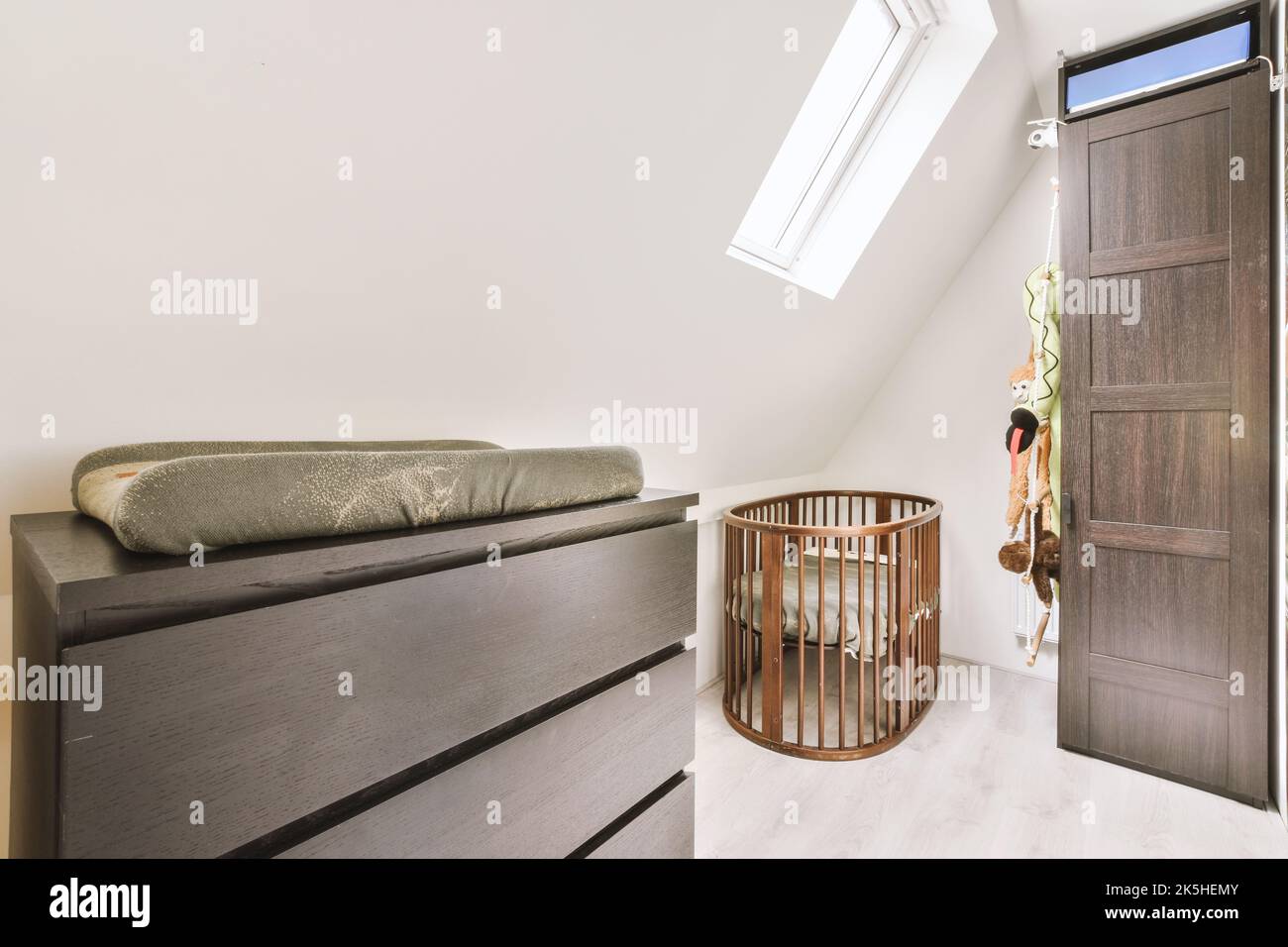 Interior of white mansard room with baby crib near window with shelves