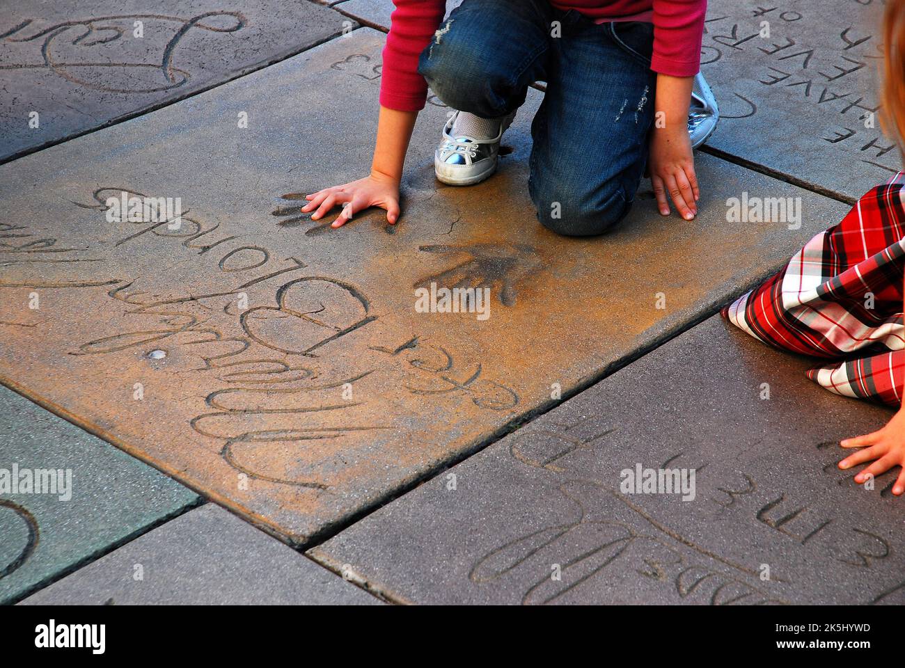 A woman sizes her hands in the handprints of movie star Marylin Monroe in the cement courtyard and plaza of Grauman's Chinese Theater in Hollywood Stock Photo