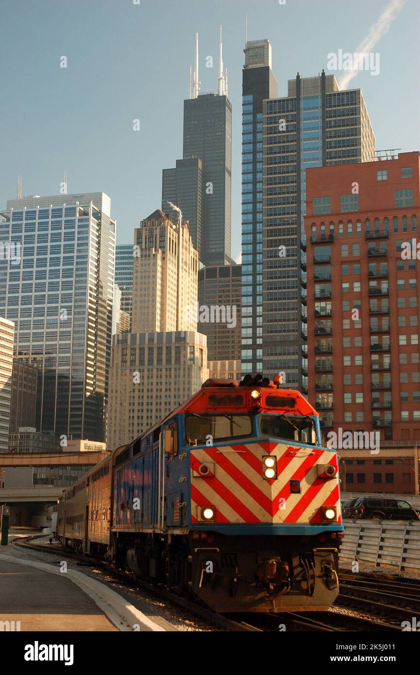A Metra Commuter train rolls past the Chicago skyline on a sunny day carrying passengers to the suburbs on the railroad Stock Photo