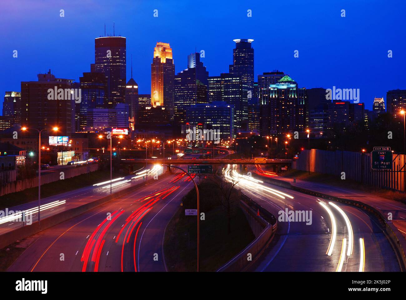 Traffic moves to and from the downtown skyline of Minneapolis, Minnesota, traveling along the interstate highway to the city center at night Stock Photo