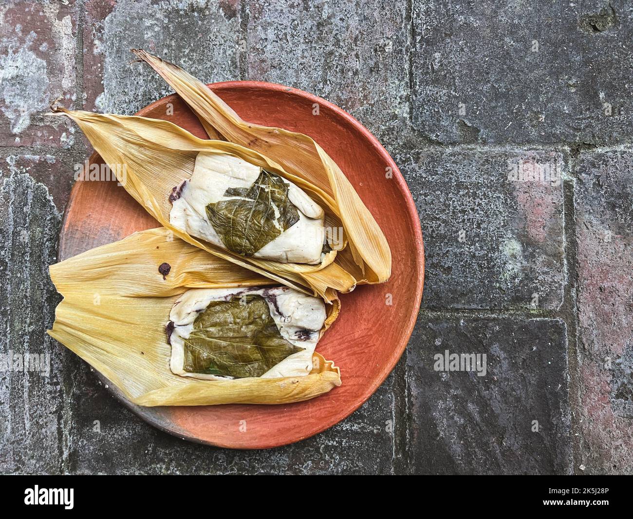 Two Oaxacan tamales on a clay plate made with hoja santa and filled ...