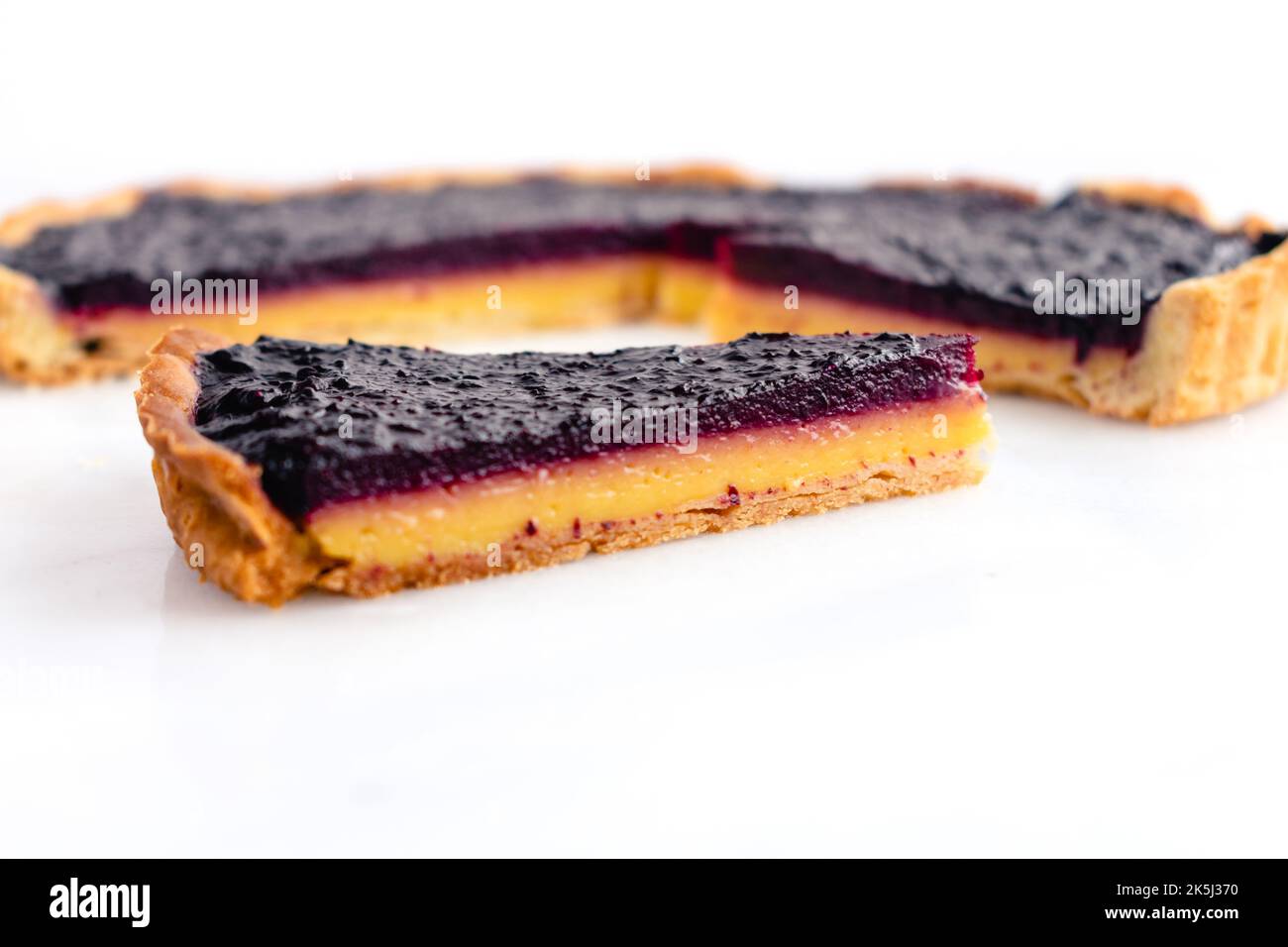 Sliced Blueberry–Lemon Curd Tart Viewed from the Side: Layered blueberry-lemon tart on a white marble background Stock Photo