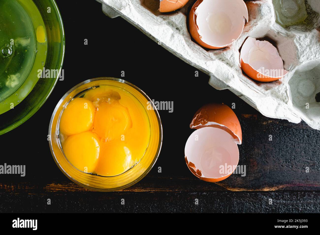 Separated Egg Yolks in a Glass Bowl on a Wooden Table: Egg yolks, egg whites, and egg shells on a dark wood background Stock Photo