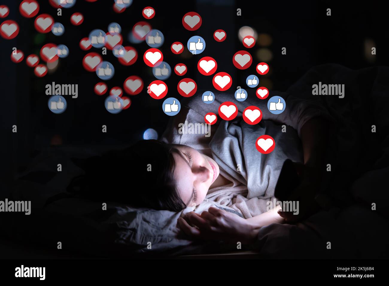 Girl with phone at night, receives hearts and likes. Stock Photo