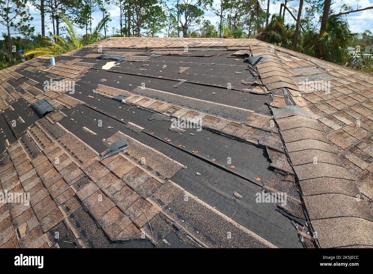 Damaged house roof with missing shingles after hurricane Ian in Florida