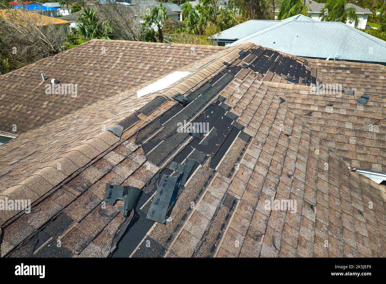 Damaged house roof with missing shingles after hurricane Ian in Florida