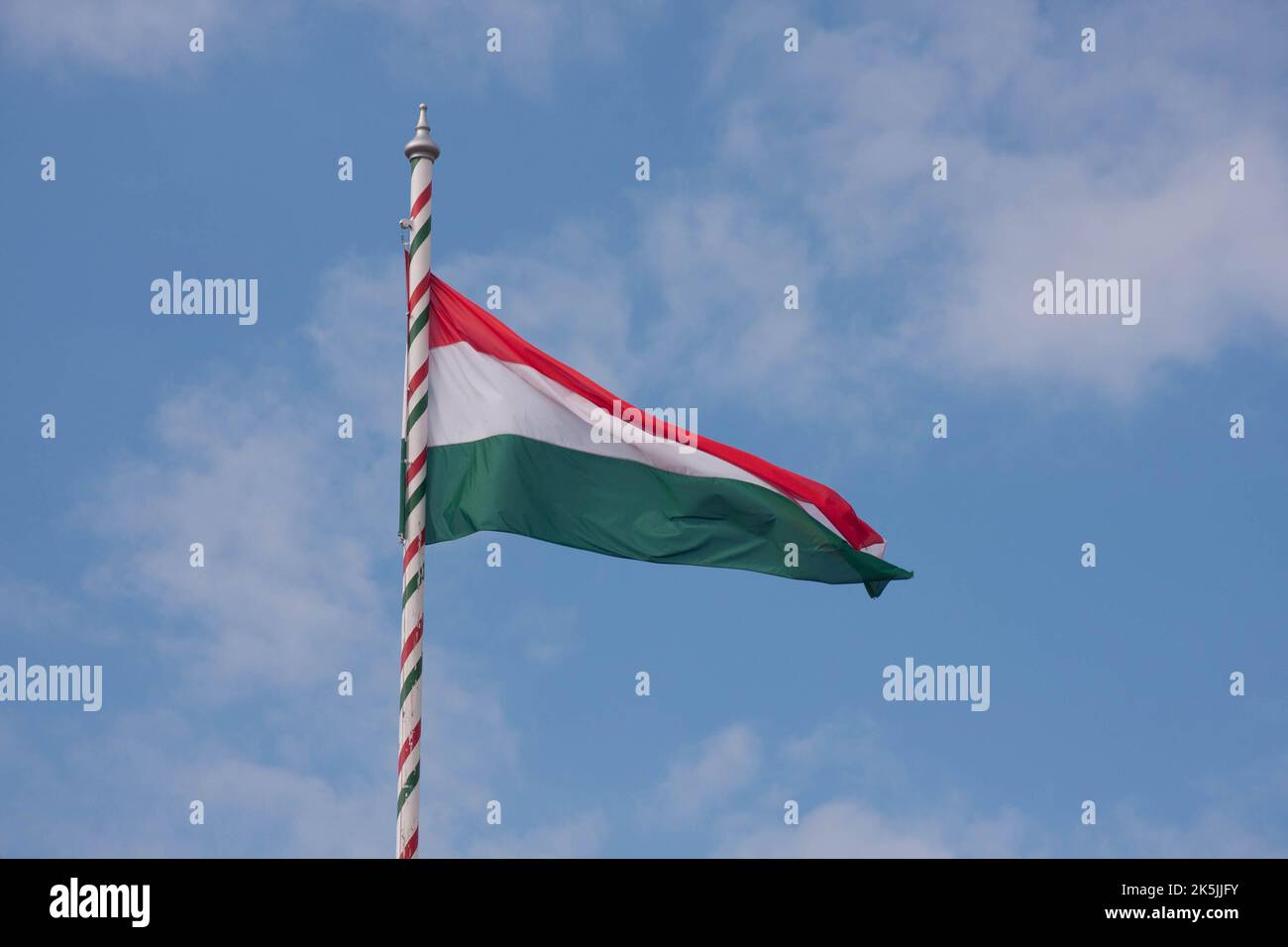 A closeup shot of the flag of Hungary against a background of cloudy blue sky Stock Photo