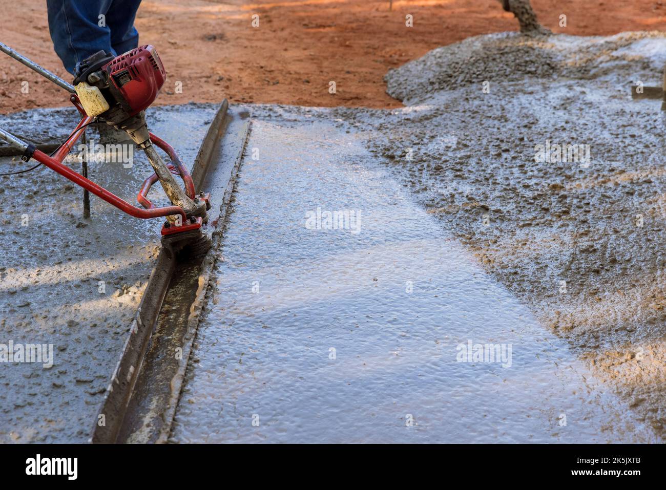 New driveway construction involves the use machine to align fresh concrete compacted layer level Stock Photo