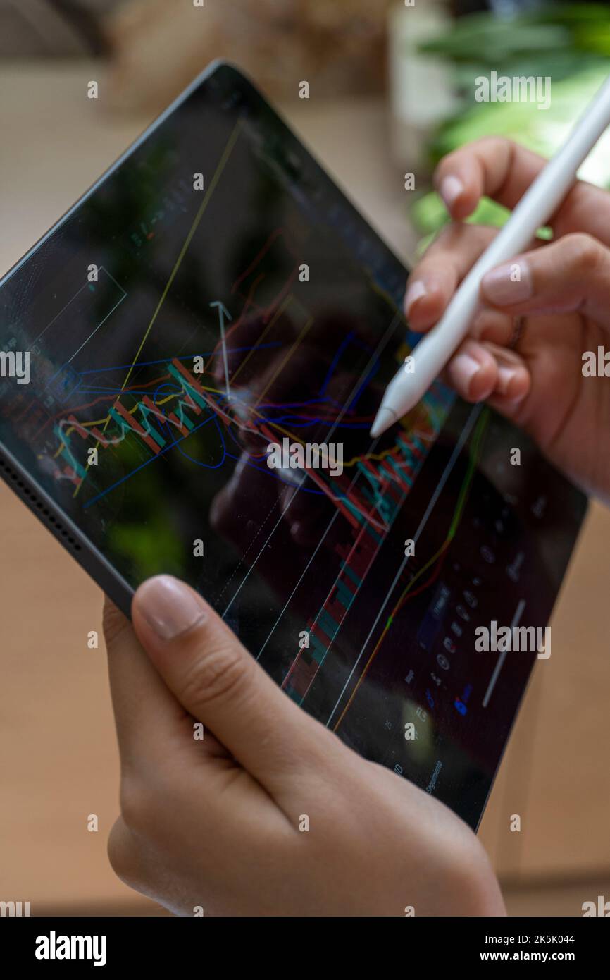 young woman, watching the stock market on her tablet, while drawing on the chart Stock Photo