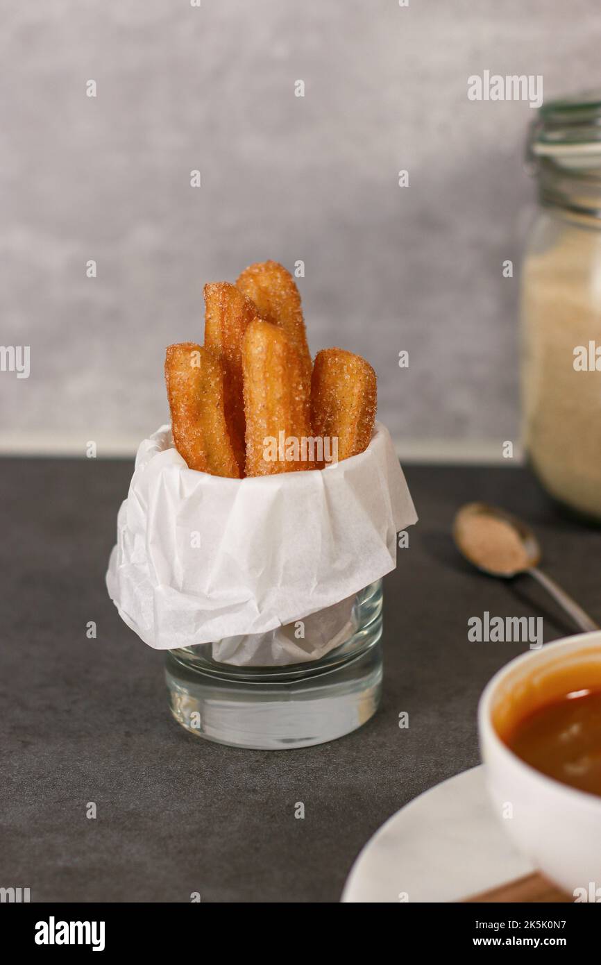 Churros with sugar and caramel sauce in a glass, grey table with copy space Stock Photo
