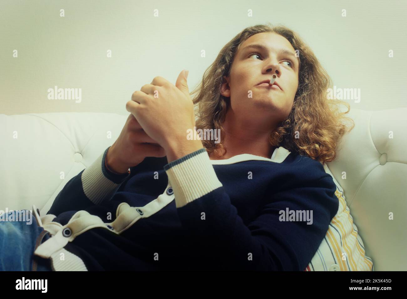 Lighting up. A handsome young man lighting a cigarette, while sitting on a sofa. Stock Photo