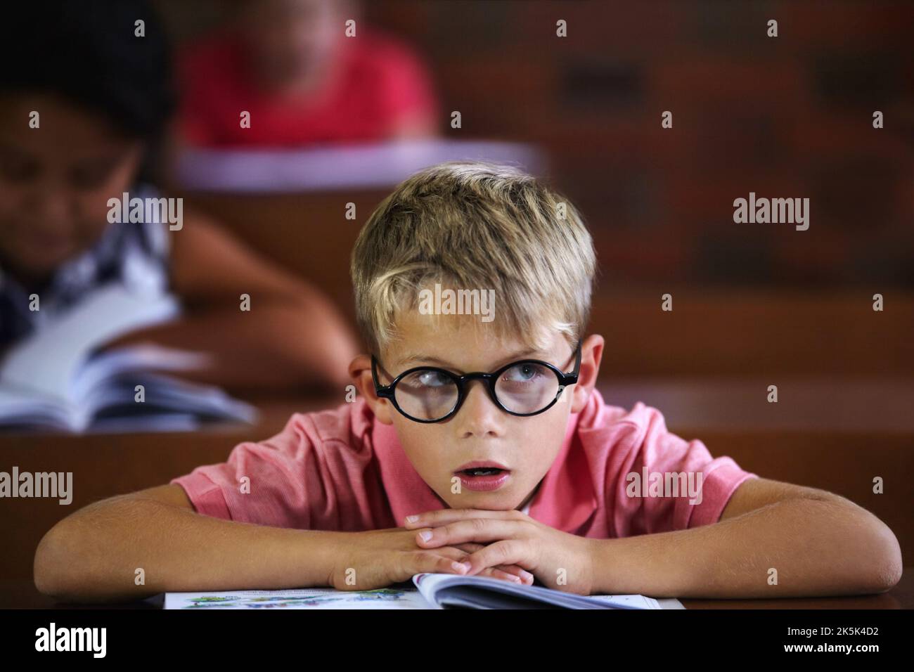 Daydreaming when he should be working. Young boy feeling overcome with boredom in the classroom. Stock Photo