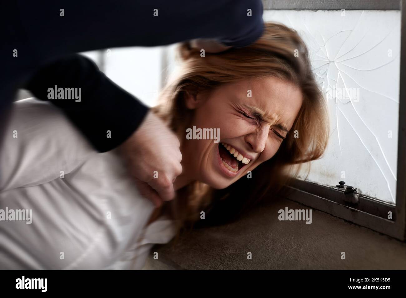 Act of violence. Abused young woman with her head being smashed against a window by an attacker. Stock Photo