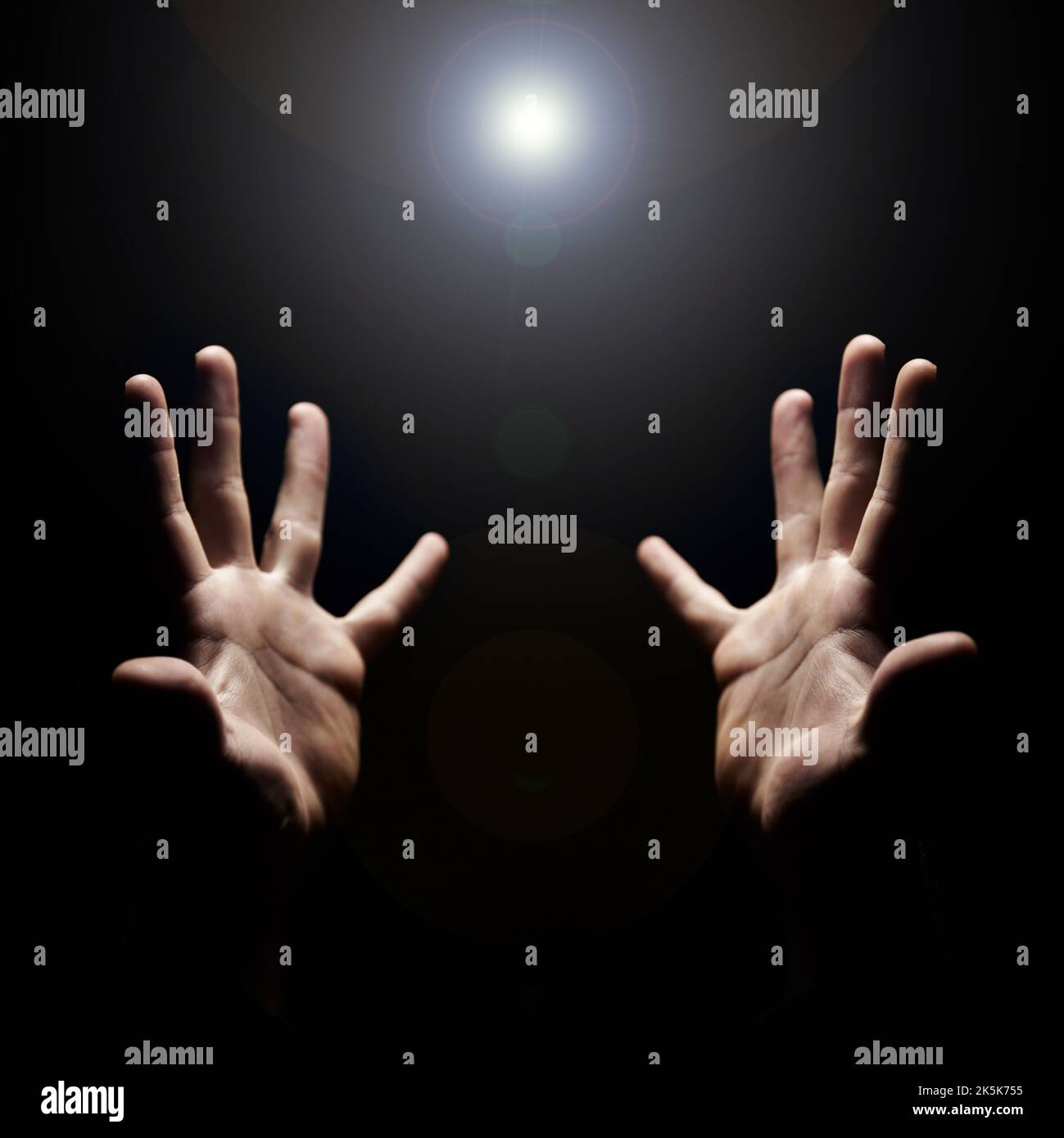 Receptive to Gods presence. Hands stretched out and open towards a light in praise. Stock Photo