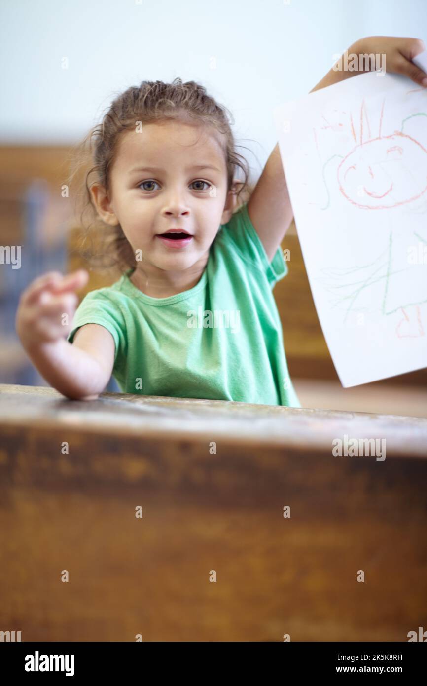 Look at my drawing. Cute little girl sitting at a school desk and