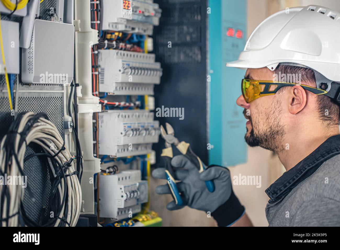 Man, an electrical technician working in a switchboard with fuses. Stock Photo