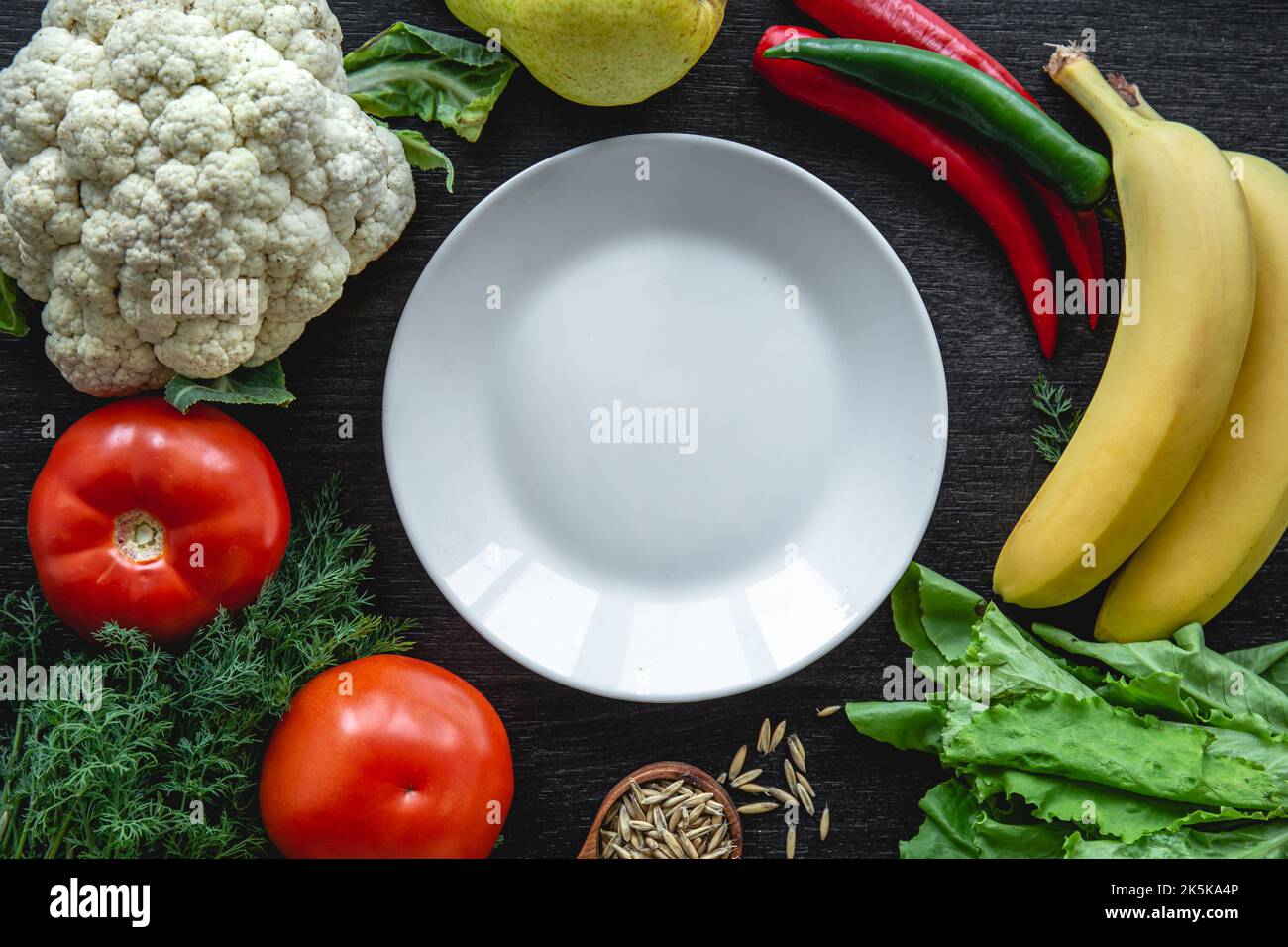 Vegetables on black background, flat lay composition with empty plate. Stock Photo