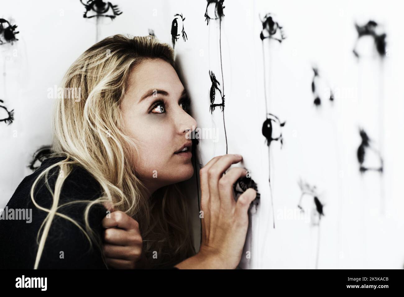 Theyre everywhere...Studio shot of a paranoid young woman looking at painted eyes on a wall. Stock Photo