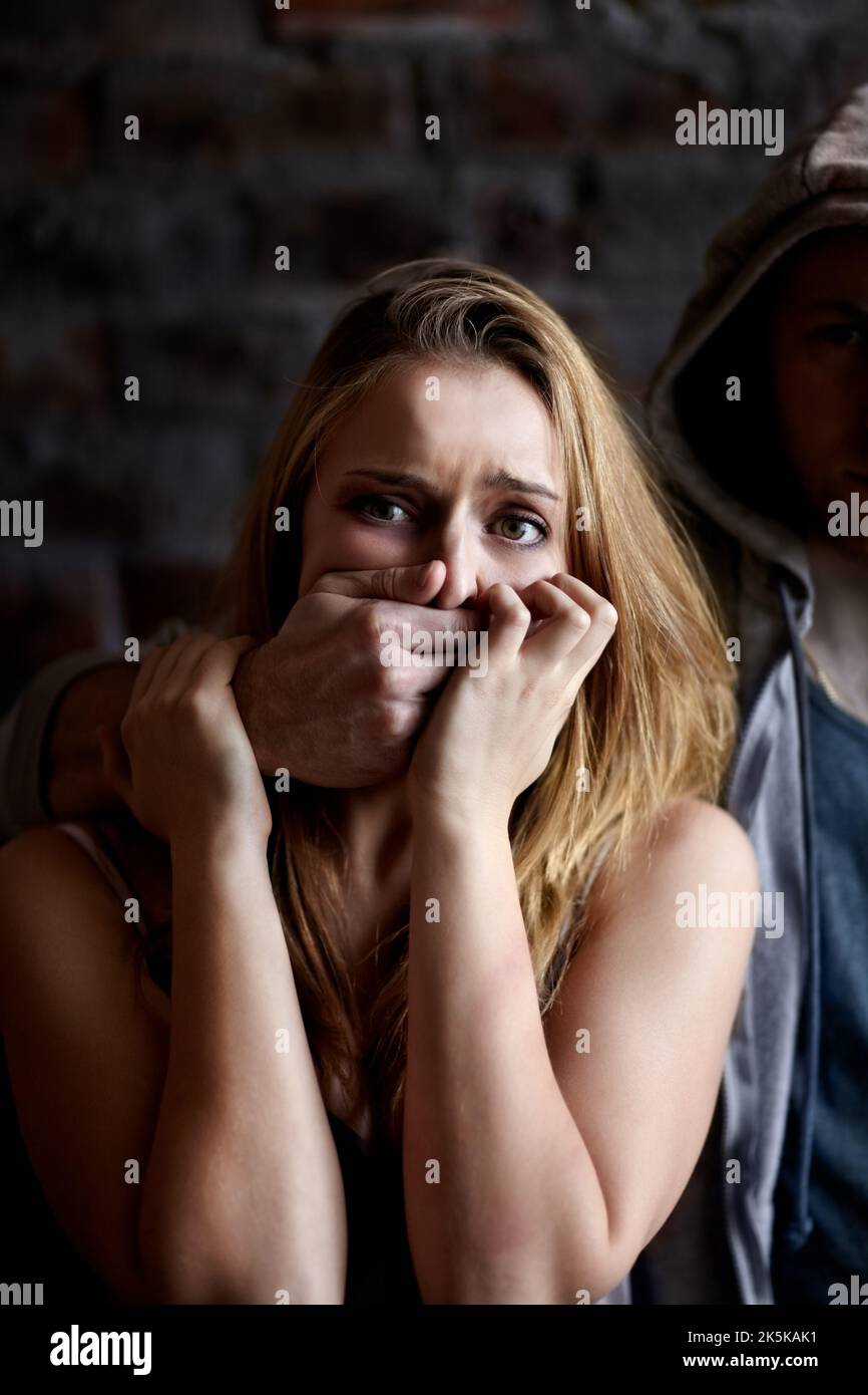 Silenced by fear and force. Abused young woman being silenced by her abuser. Stock Photo