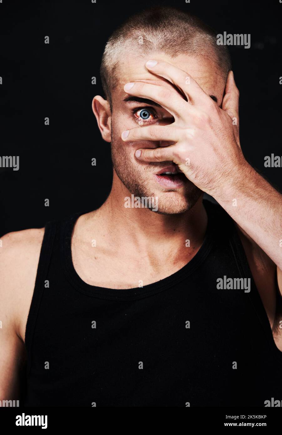 Can you see me. Portrait of a paranoid young man peeking through his fingers. Stock Photo