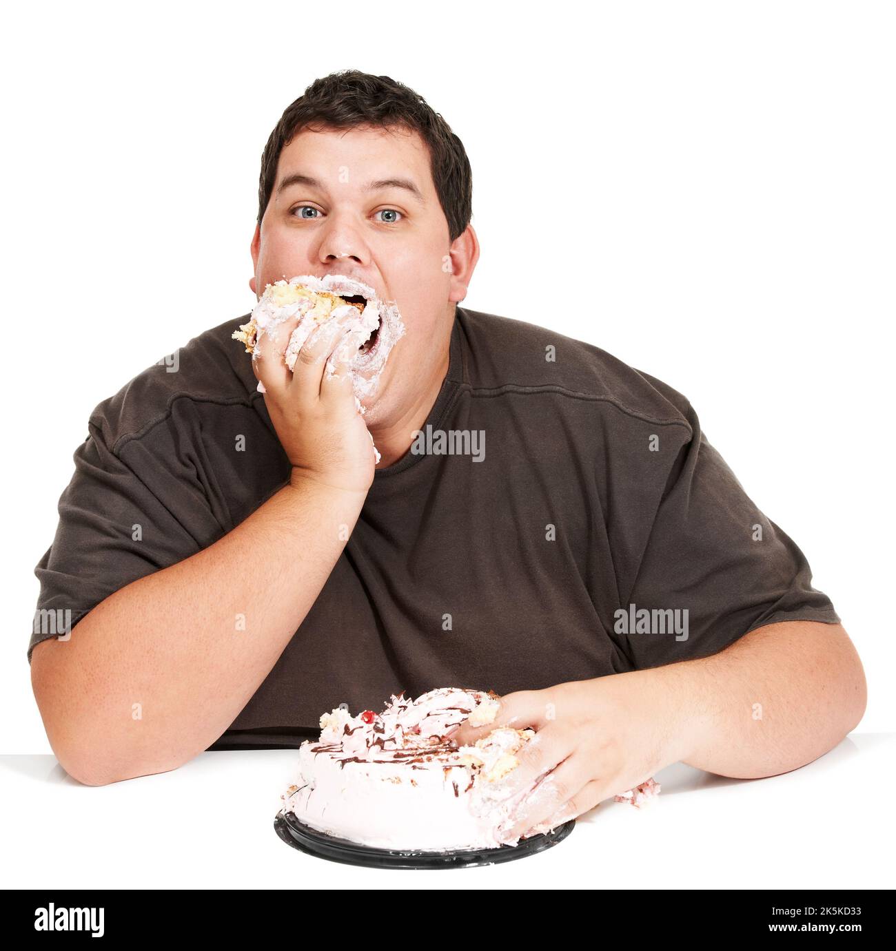 Eating cake in record time. An obese young man stuffing a cake down his face and not being too dainty about it. Stock Photo