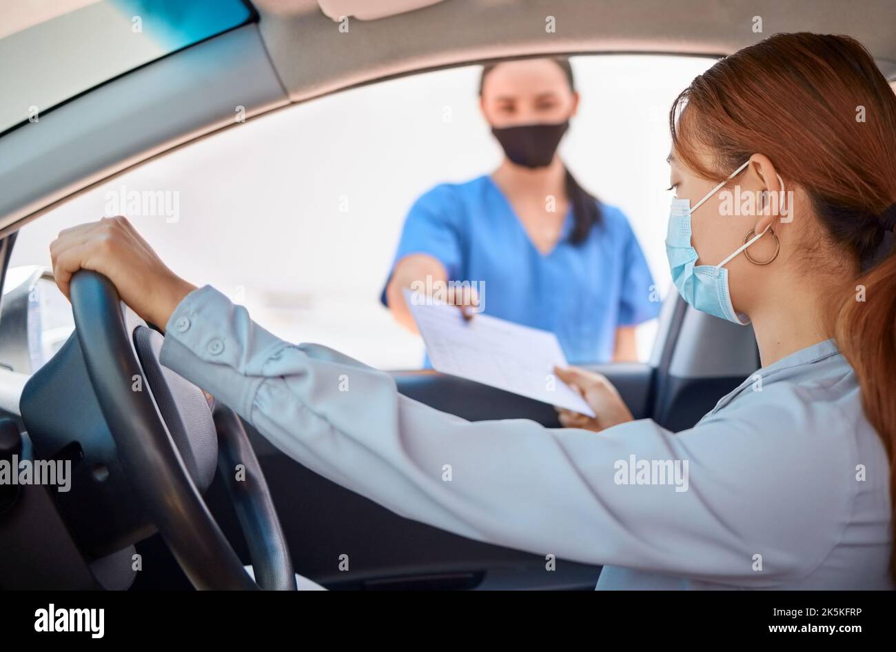 Covid test in car and drive thru, nurse giving patient forms to fill in. Woman in vehicle wearing a mask and taking documents from medical worker Stock Photo