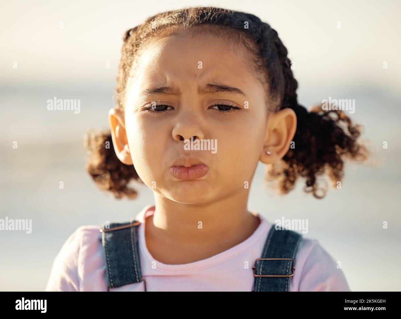 Portrait, sad and face of an unhappy little girl feeling lonely or upset against a blurred background. Closeup of an emotional African female child Stock Photo