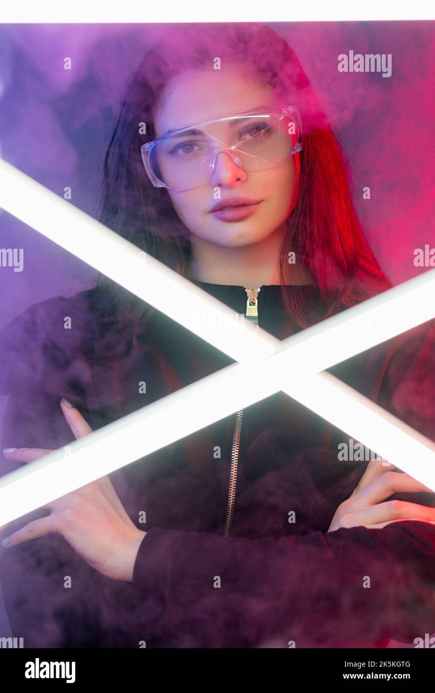 Cyberpunk portrait. Future portal. Vaporwave party. Confident woman in goggles with crossed arms in pink purple neon light color smoke with white LED Stock Photo