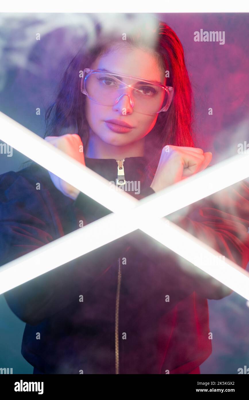 Neon portrait. Cyberpunk hero. Futuristic combat. Fantastic woman in glasses with crossed fists gesture in pink purple neon light steam with white LED Stock Photo