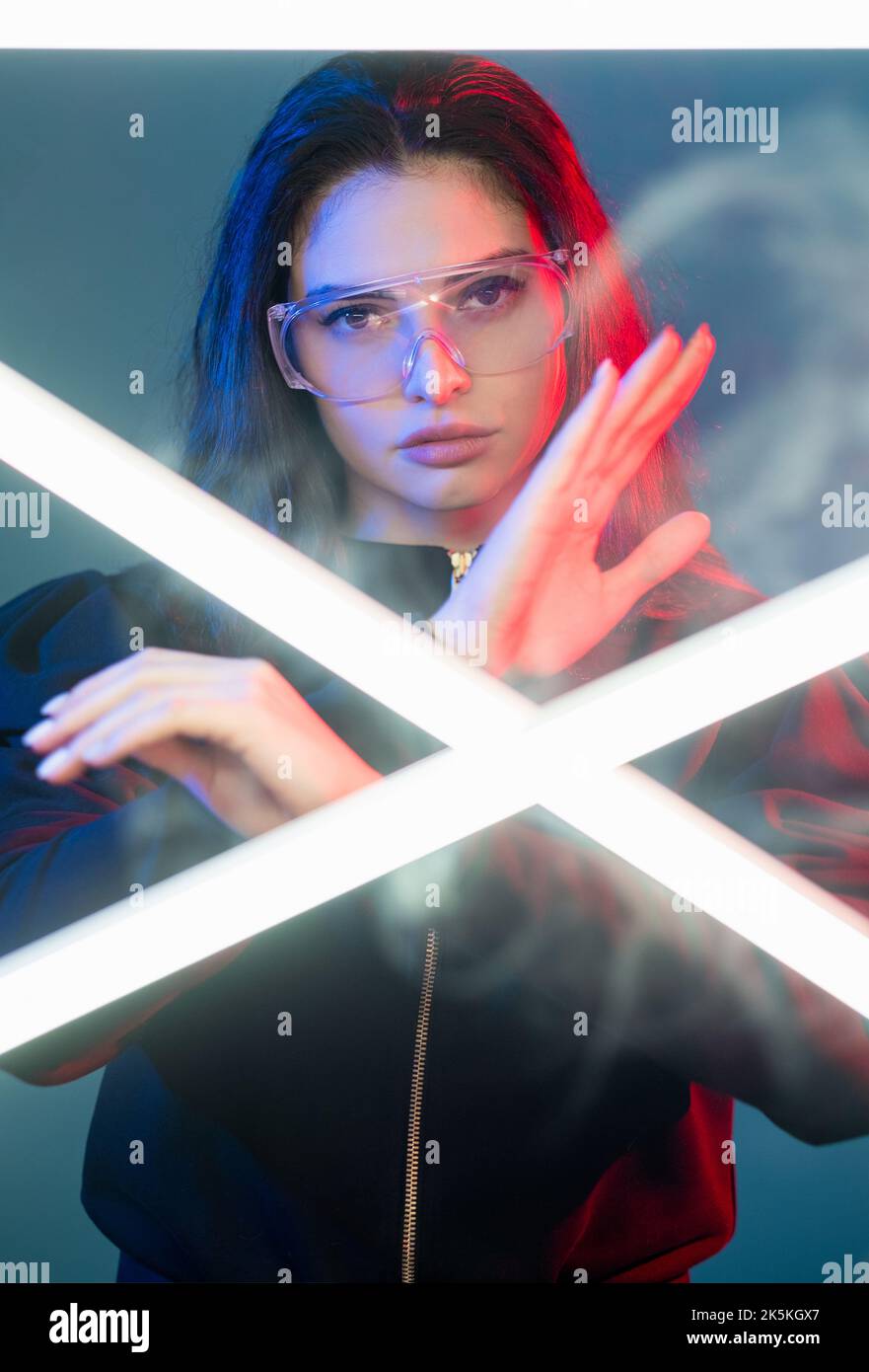 Cyberpunk fighter. Futuristic portrait. Galaxy war. Red neon light brave cyborg woman in glasses performing karate hand move in mist with crossed whit Stock Photo