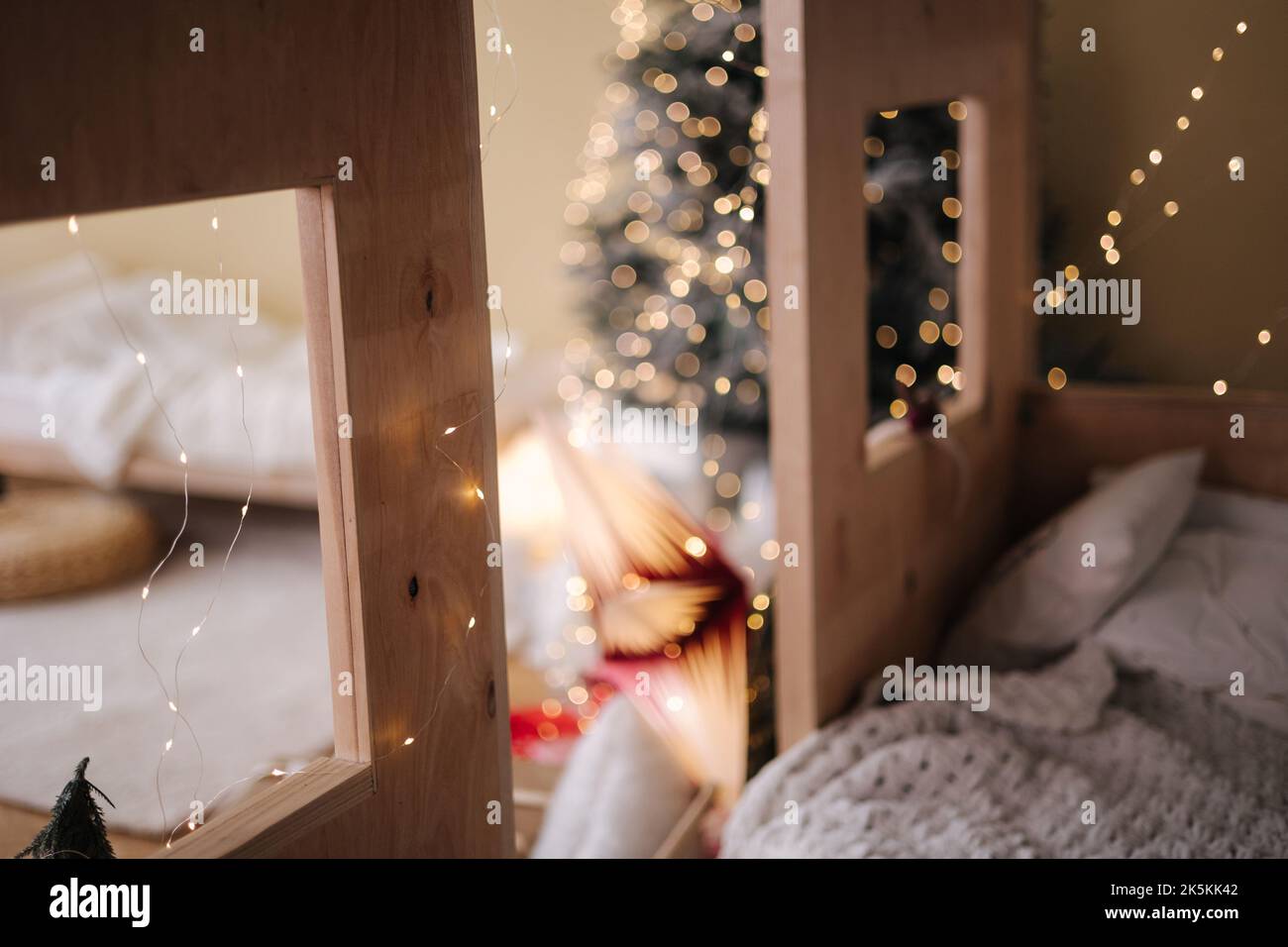 Children room with Christmas decorations. Presents in red festive packaging. Interior design for kids. Background of christmas tree lights. Stock Photo