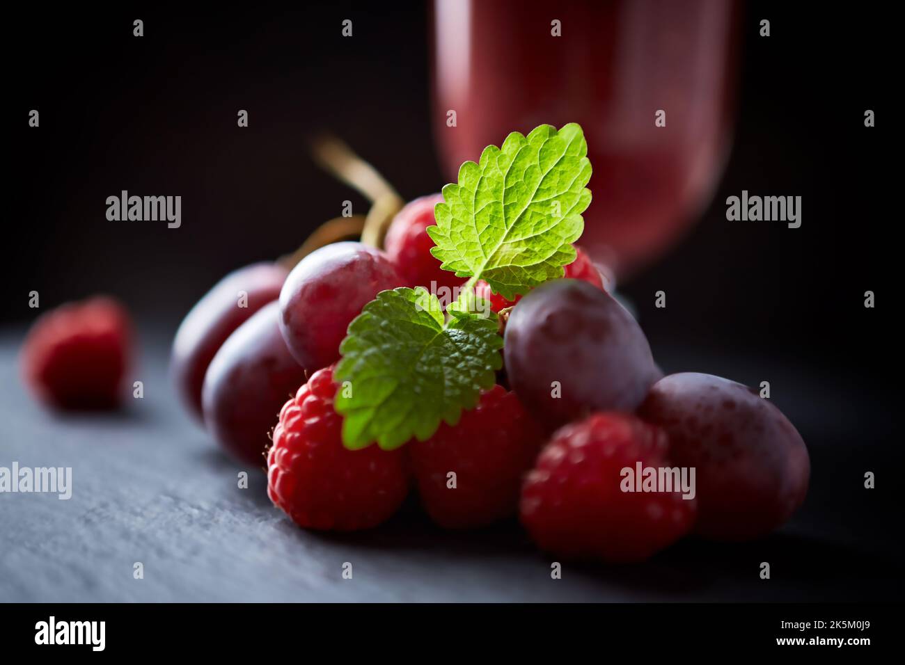 Grape And Raspberry Grapes and raspberries and fresh smoothie in a glass. Dark background ...