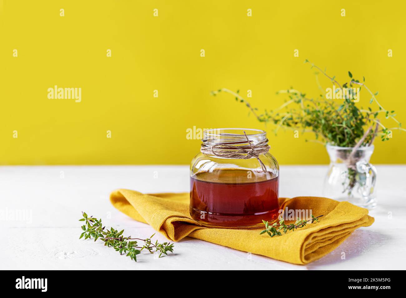 Thyme honey in small jar, fresh thyme, yellow napkin on white table with yellow background Stock Photo