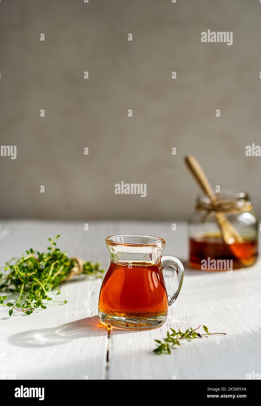 Thyme honey in small jug and jar, small thyme branch on white wooden table with grey background Stock Photo