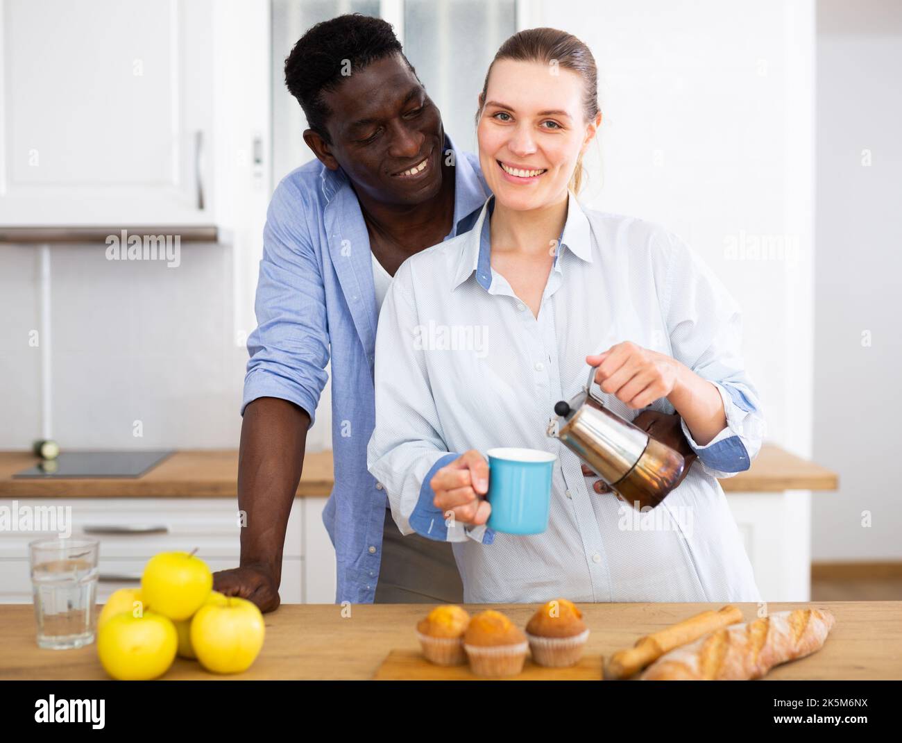 Happy biracial couple laughing and drinking coffee in morning in kitchen Stock Photo