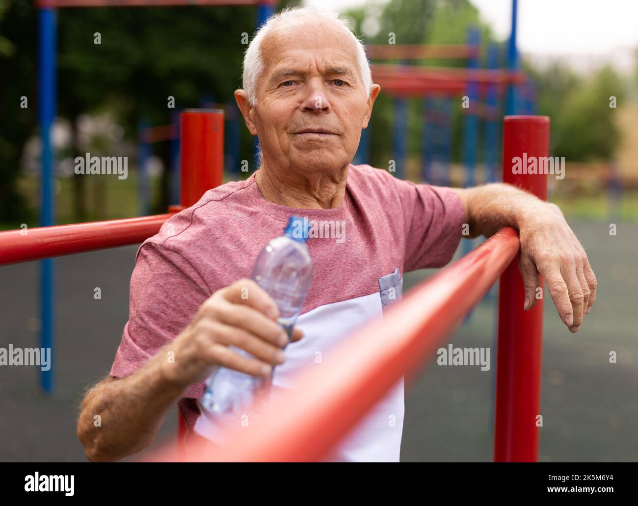 Old man with bottle of water standing in outdoor workout station Stock ...