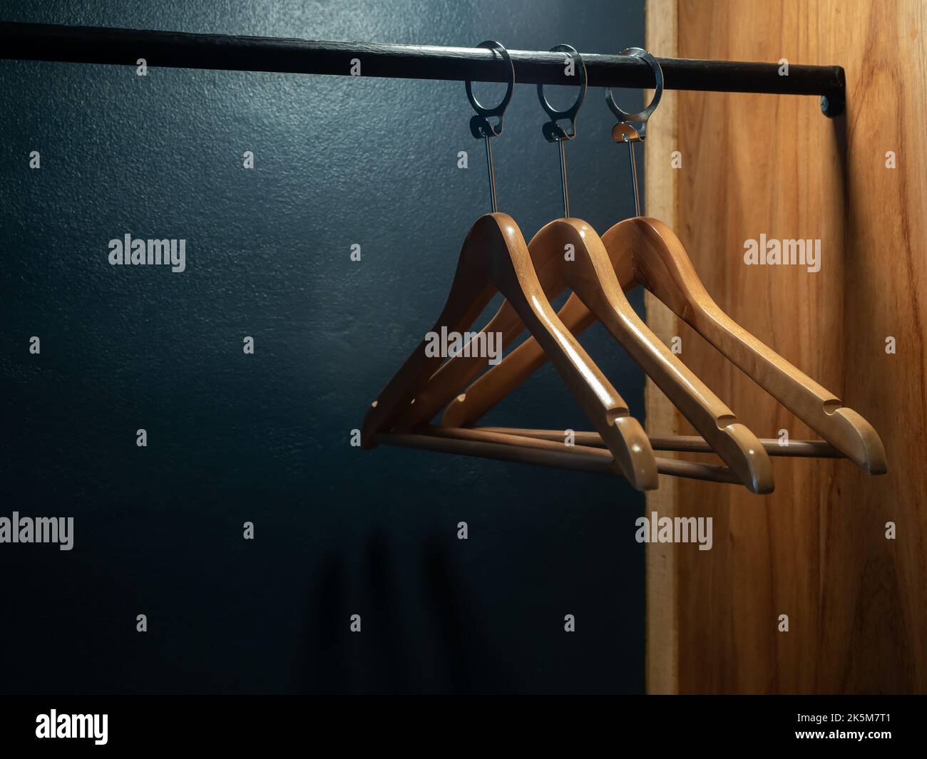 Three empty wooden clothes hangers without shirts or dress hanging on a black cloth rack in the wood wardrobe on dark blue background preparing for th Stock Photo