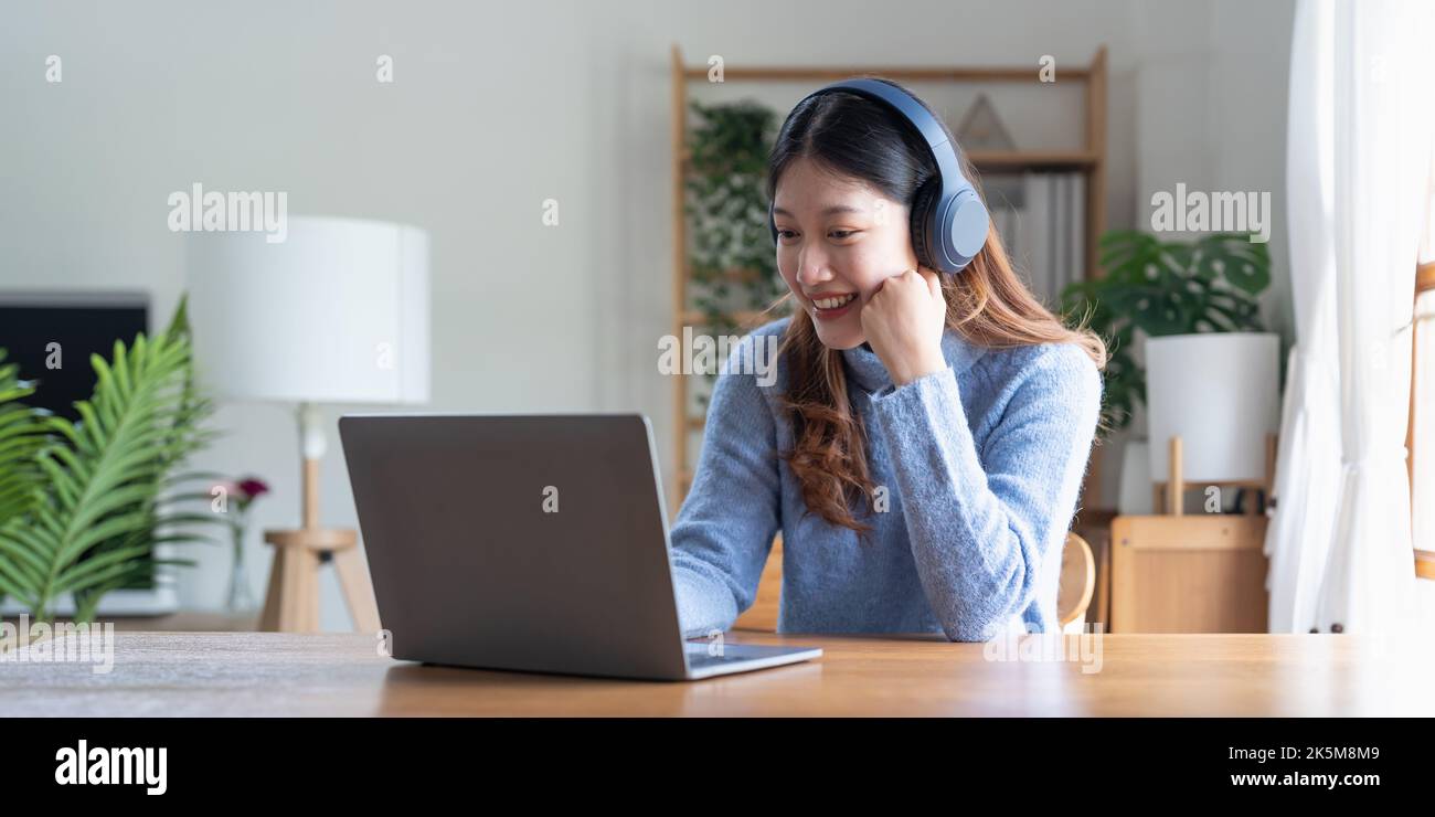 Young asian woman talk on video call at the table using headphones