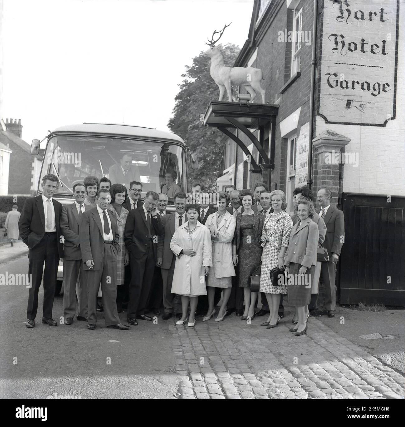 1964, historical, happy people, smartly dressed, gathered outside the White Hart Hotel on Exchange Street, Aylesbury, Bucks, for a group photo before their coach trip on an away day. Stock Photo