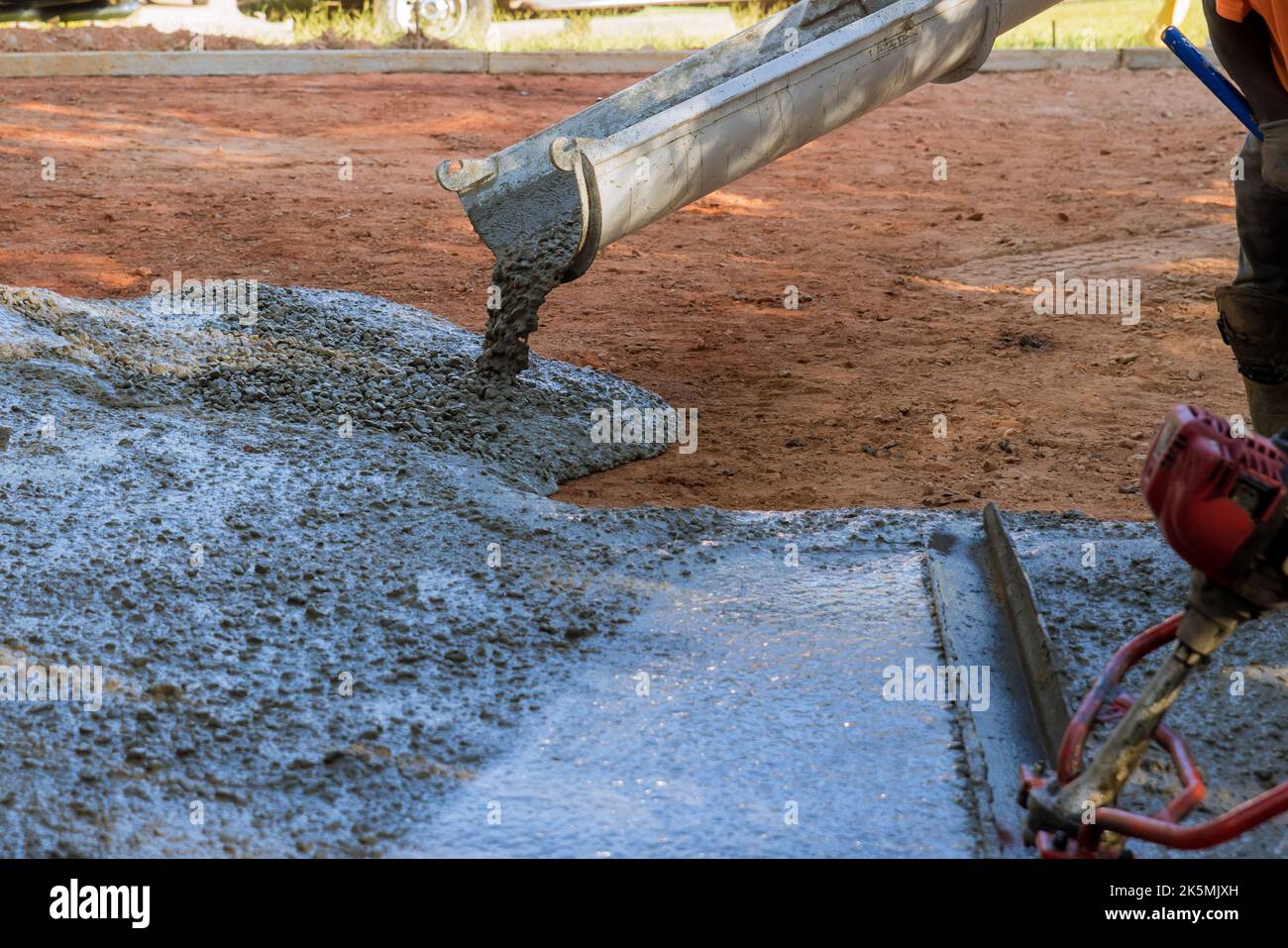 An employee is pouring wet concrete at new construction site on near new home to pave a driveway