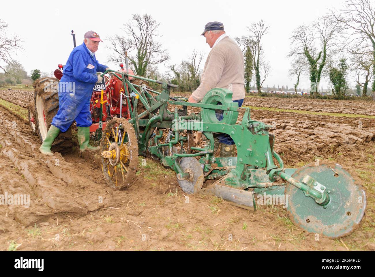 Two farmers change the settings on a vintage plough, attached to an old Massey Ferguson tractor