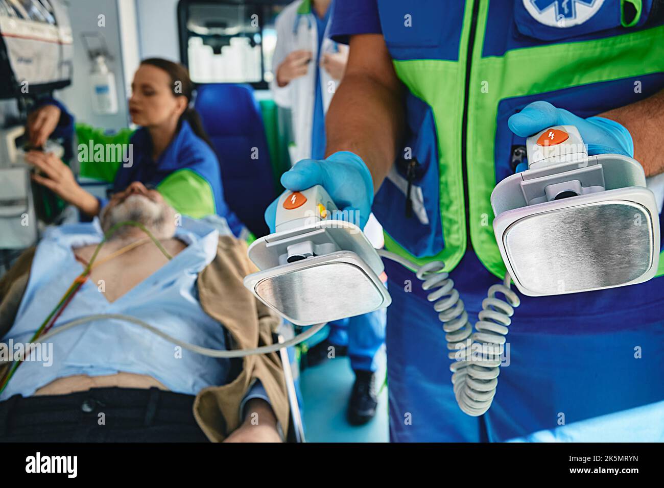 Paramedic preparing defibrillator for cardiopulmonary resuscitation of unconscious patient in ambulance to save his life and transportation him to hos Stock Photo